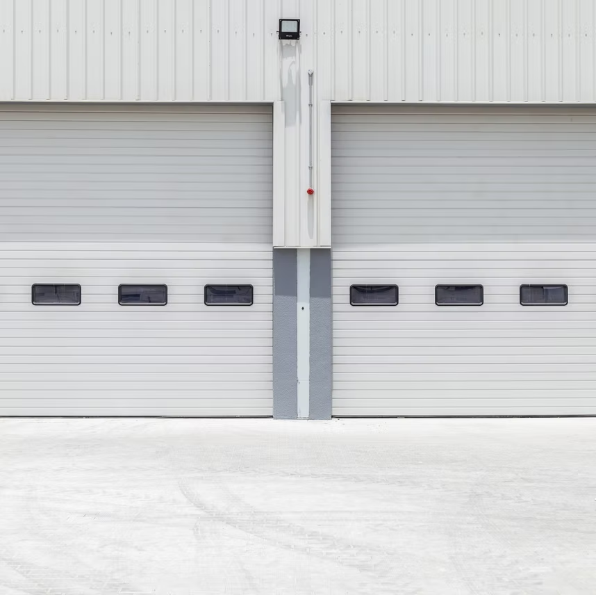 Two light-gray industrial roller shutter garage doors with small rectangular windows, separated by a central wall section.