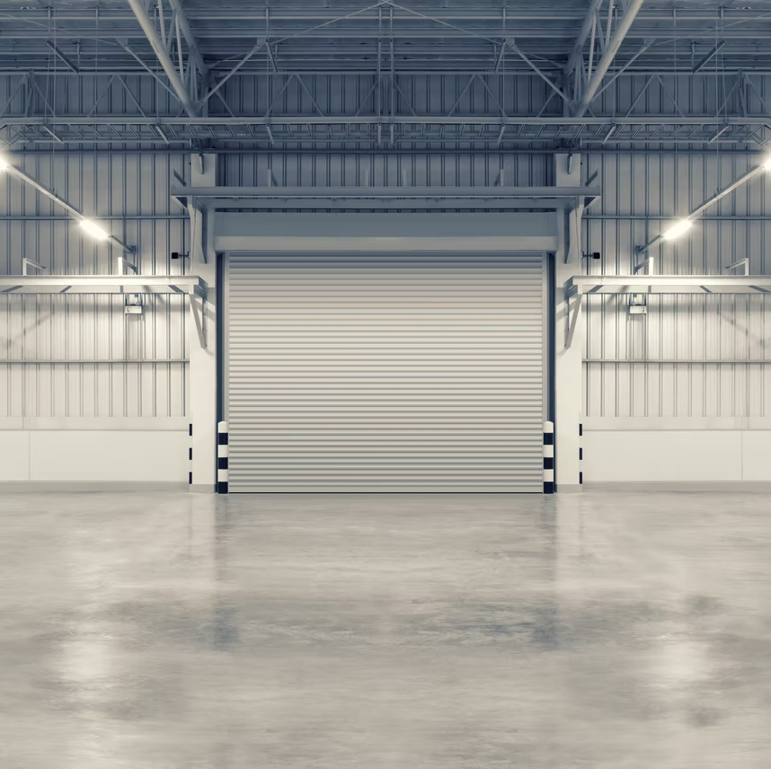 A large, closed metal rolling garage door inside a spacious, brightly lit warehouse with a concrete floor.