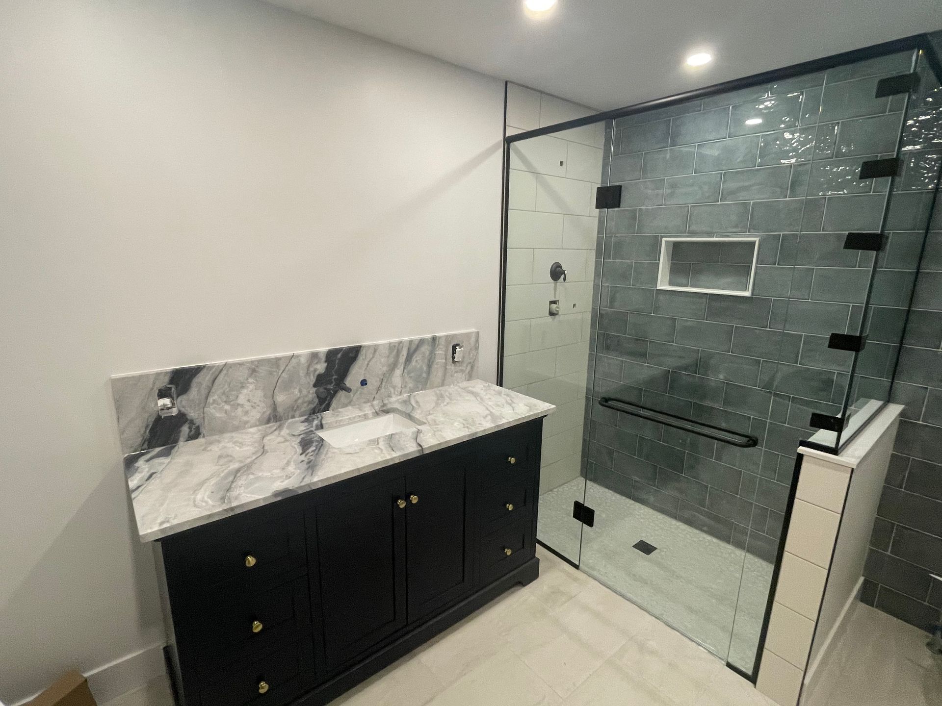 Bathroom with black vanity, marble countertop, glass shower enclosure, and gray tile.