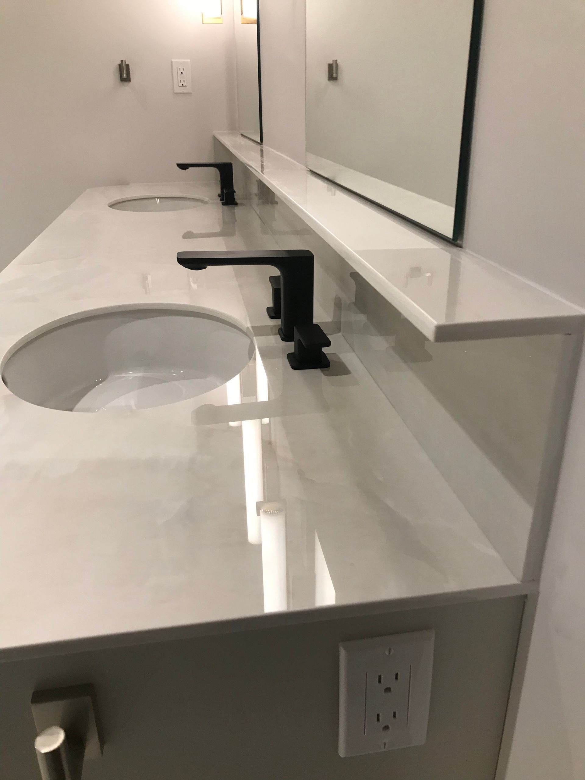 Bathroom with three sinks, black faucets, and a white countertop. Mirrors and light fixtures are visible.