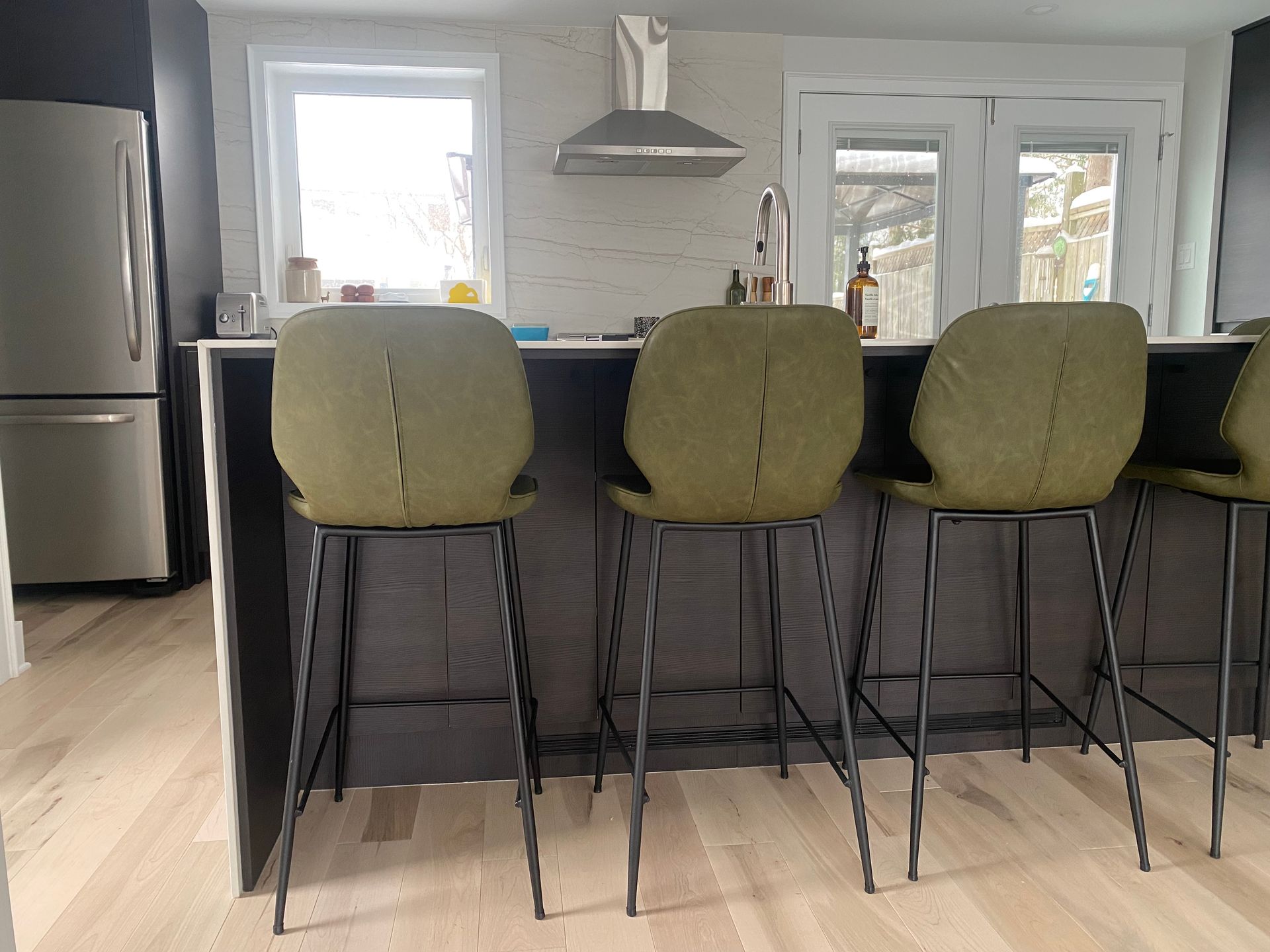 A kitchen with green bar stools and a stainless steel refrigerator.