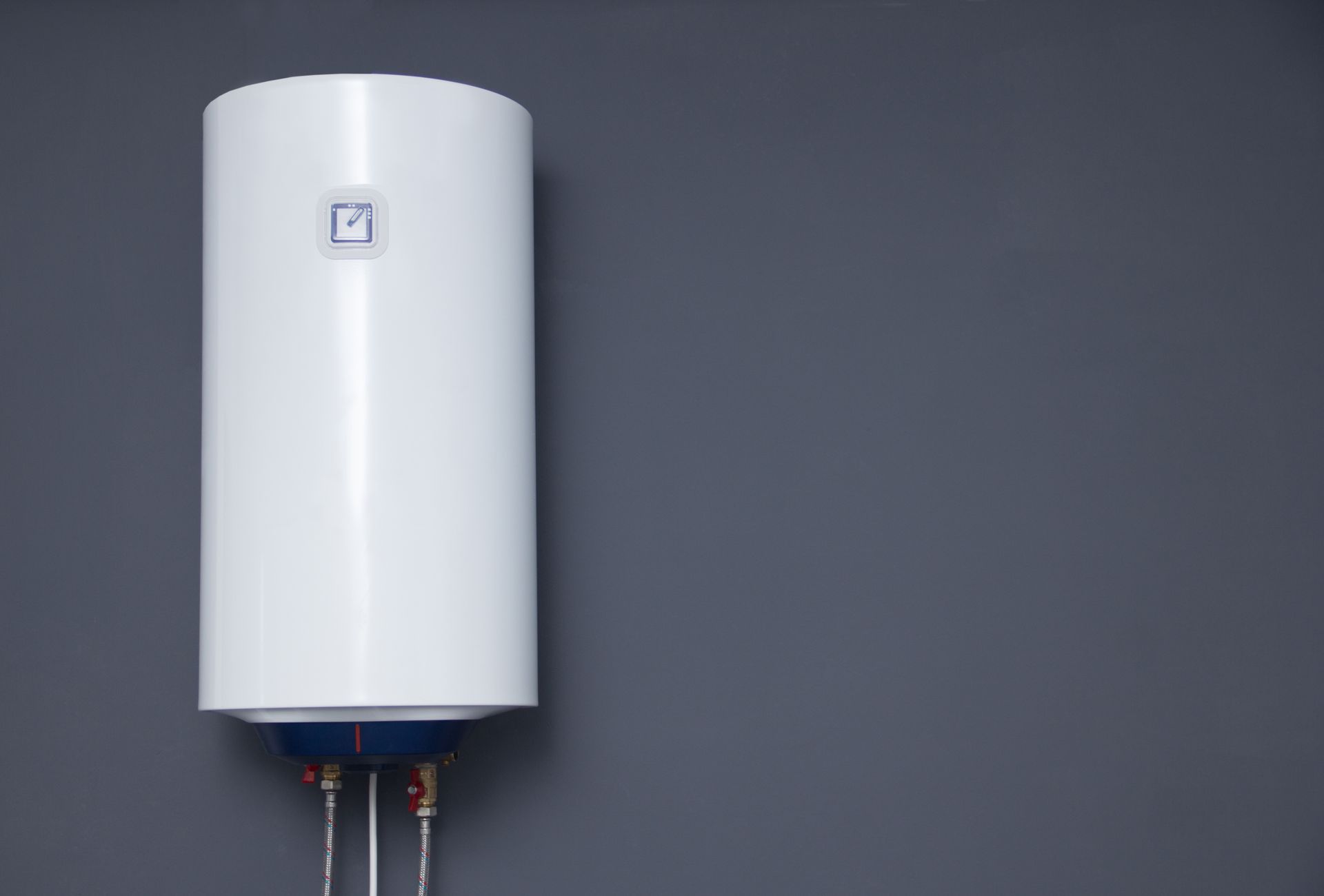 White cylindrical water heater mounted on a gray wall with exposed pipes below