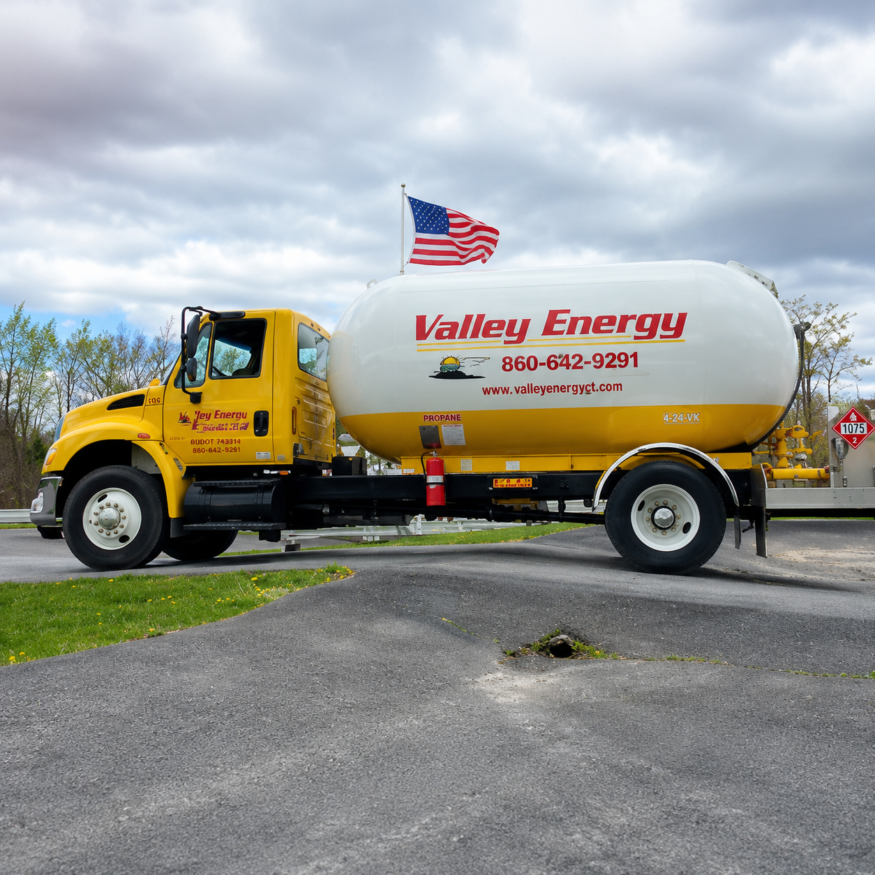 A yellow tanker truck is parked in front of several large, cylindrical storage tanks under a cloudy sky.