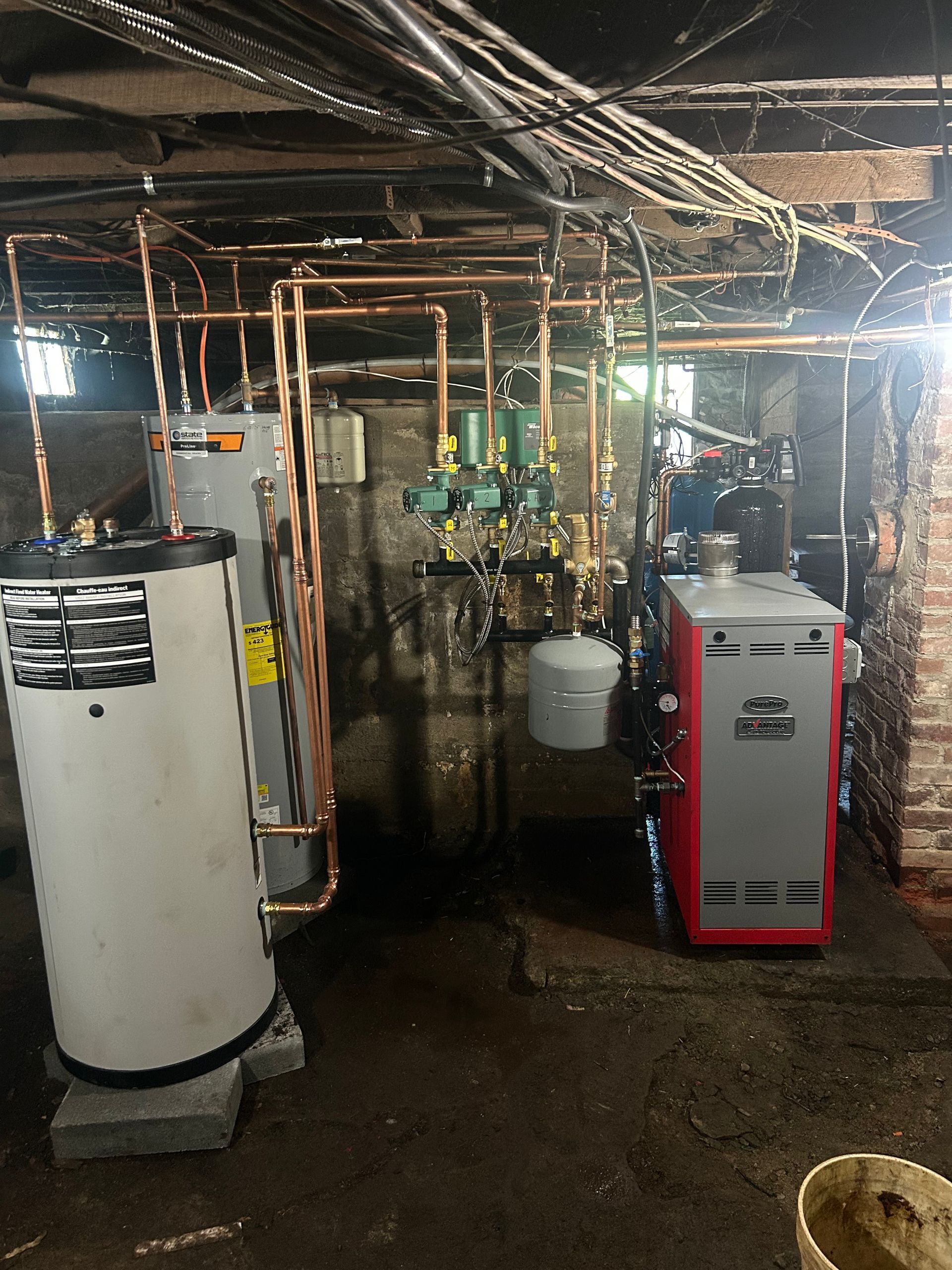 Five colorful gas cylinders in red, green, blue, tan, and brown, secured against a gray wall by a metal rack and bar.