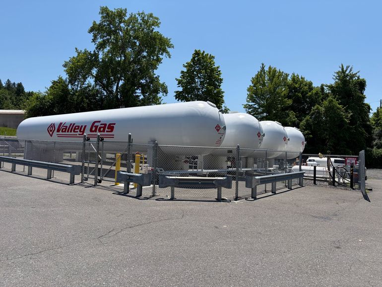 A large group of employees stands in front of two tall, white storage tanks labeled 