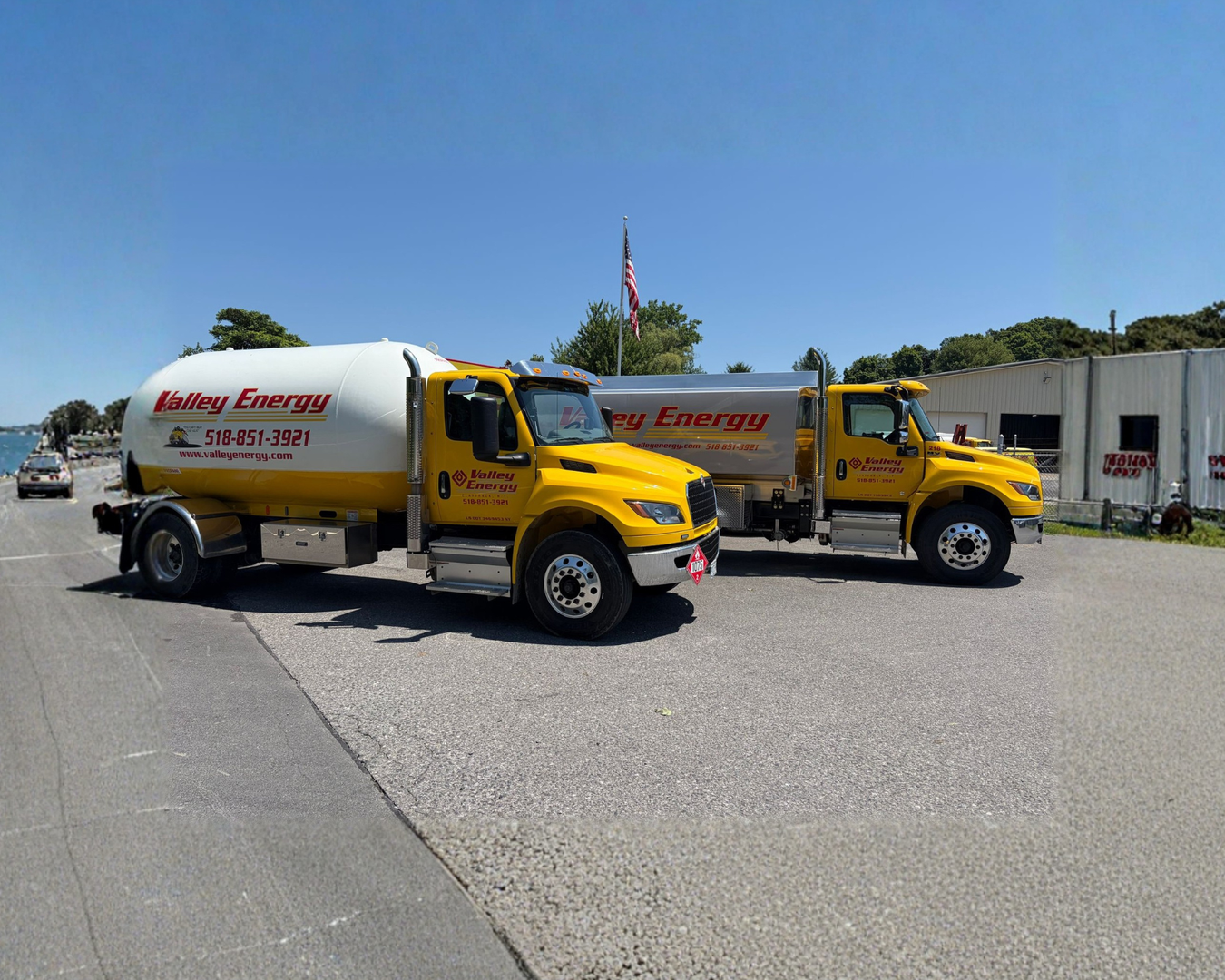 Two yellow Valley Energy tanker trucks parked on a gravel lot in front of a large, horizontal white storage tank.