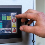 A person in a factory setting touches the screen of an industrial control panel mounted on a machine.