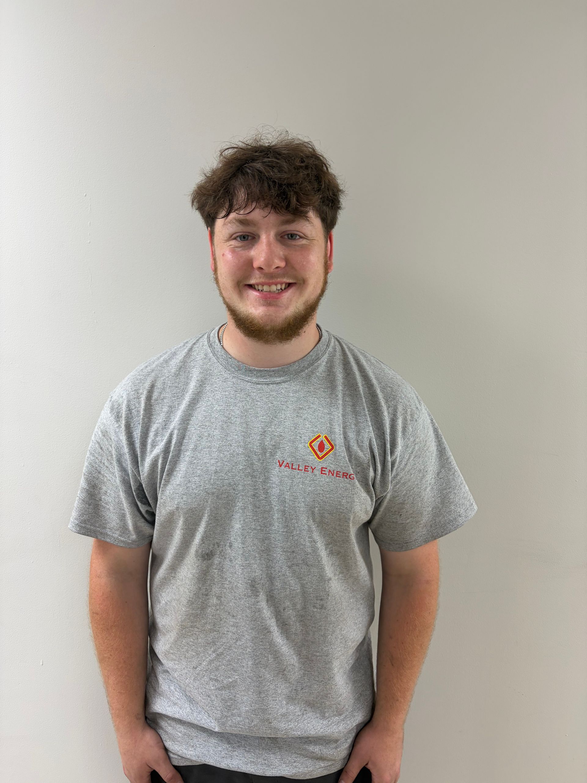 A person with short, light-brown hair and a neutral expression, wearing a light-gray collared shirt against a plain wall.