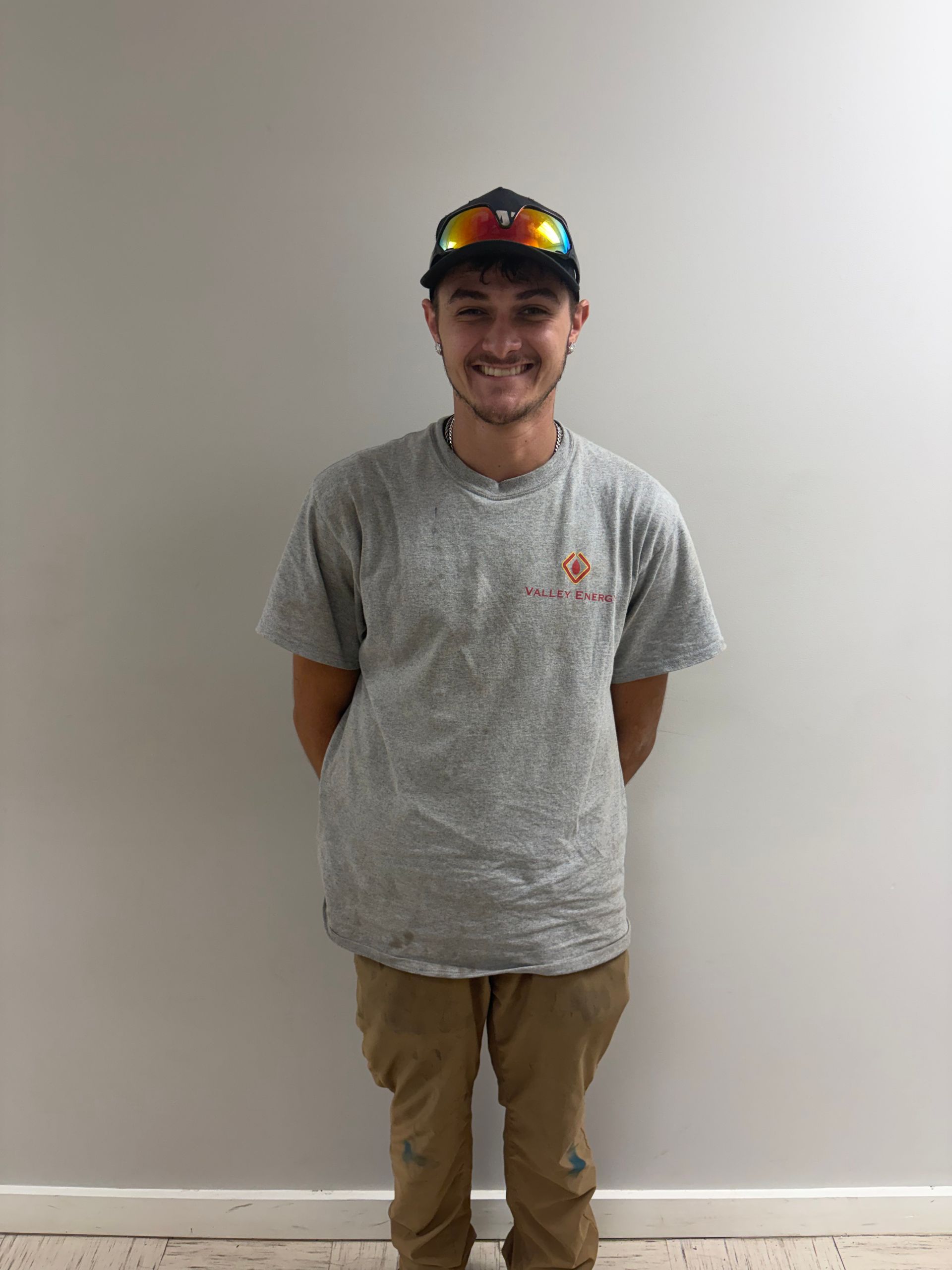 A person wearing a black baseball cap and a silver chain necklace, positioned against a plain, light-colored background.