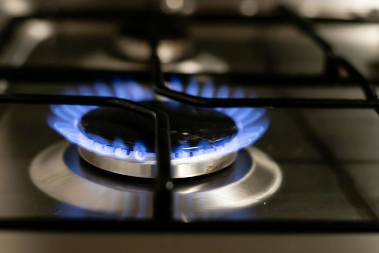 A blue flame burns on a circular gas stove burner on a stainless steel stovetop with black grates.