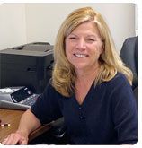 A smiling professional seated at a desk with an office printer in the background.