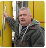 A person wearing a green jacket stands beside a bright yellow vehicle, holding onto a silver handle.