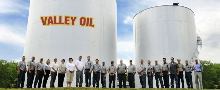 A large group of employees stands in front of two tall, white storage tanks labeled 