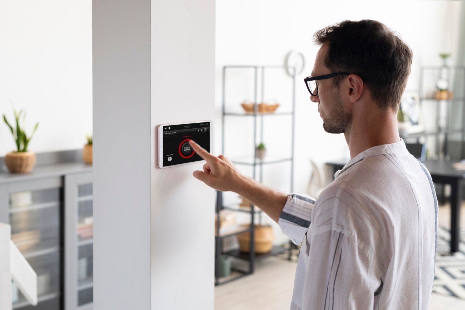 A person wearing glasses uses their finger to adjust a wall-mounted smart home control screen in a bright, modern room.
