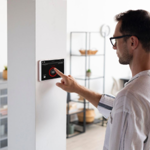 A person in a light-colored shirt touching a wall-mounted smart home control panel in a modern, well-lit living space.