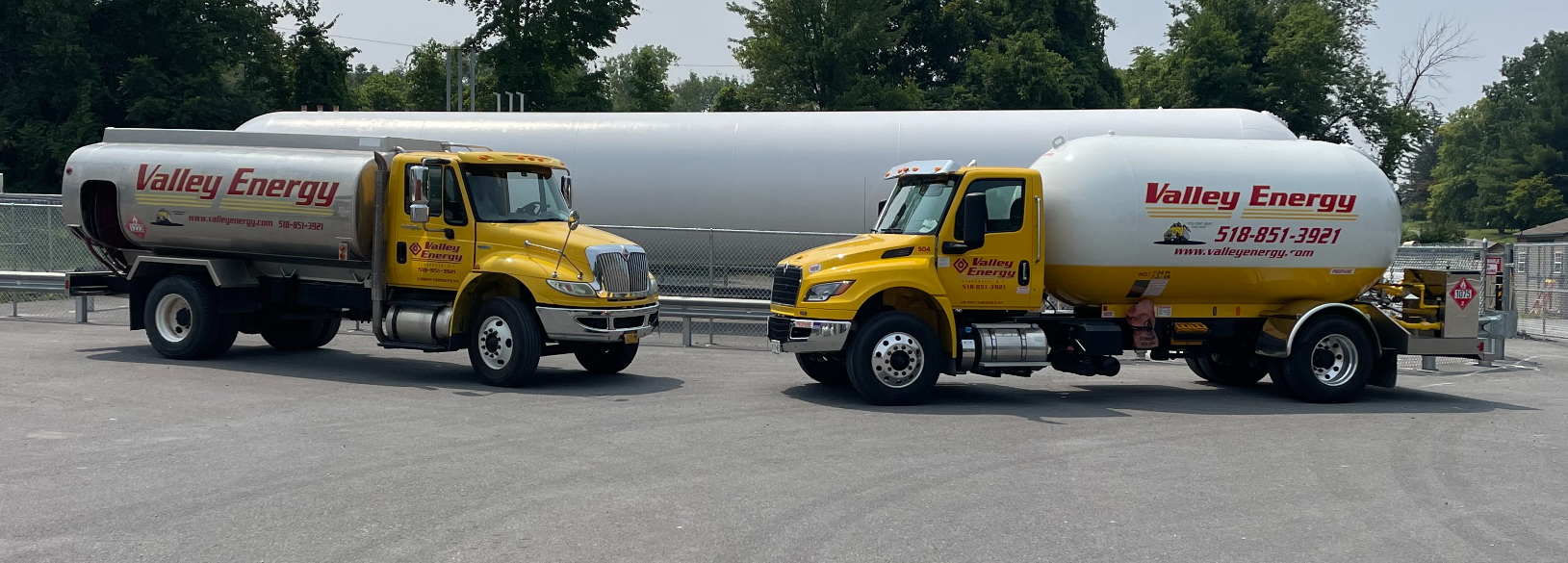 Two yellow Valley Energy tanker trucks parked on a gravel lot in front of a large, horizontal white storage tank.