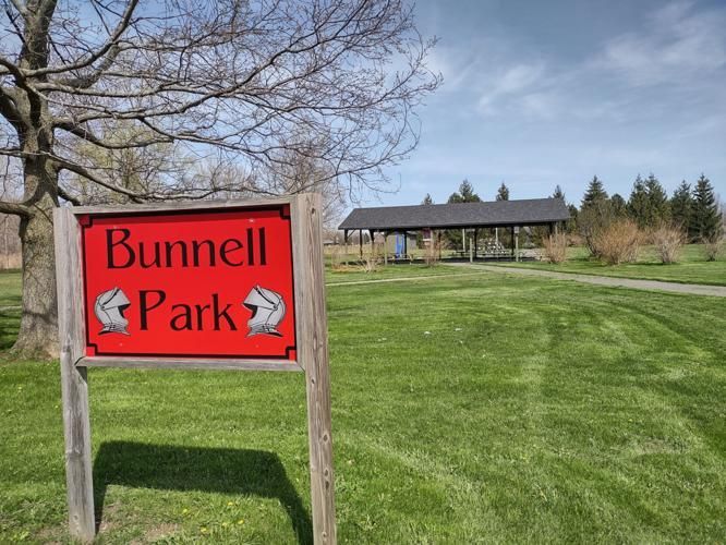 Bunnell Park sign in a grassy park with trees and a pavilion in the background