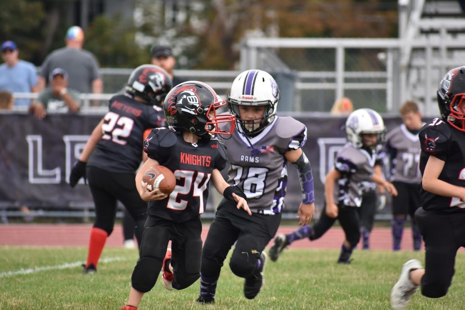 Youth football players in black and gray uniforms running with the ball on a grassy field