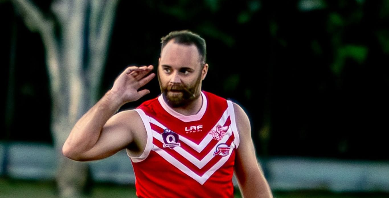 A senior mens player during a game, looking at the crowd with his hand behind his ear asking in gesture if they heard him