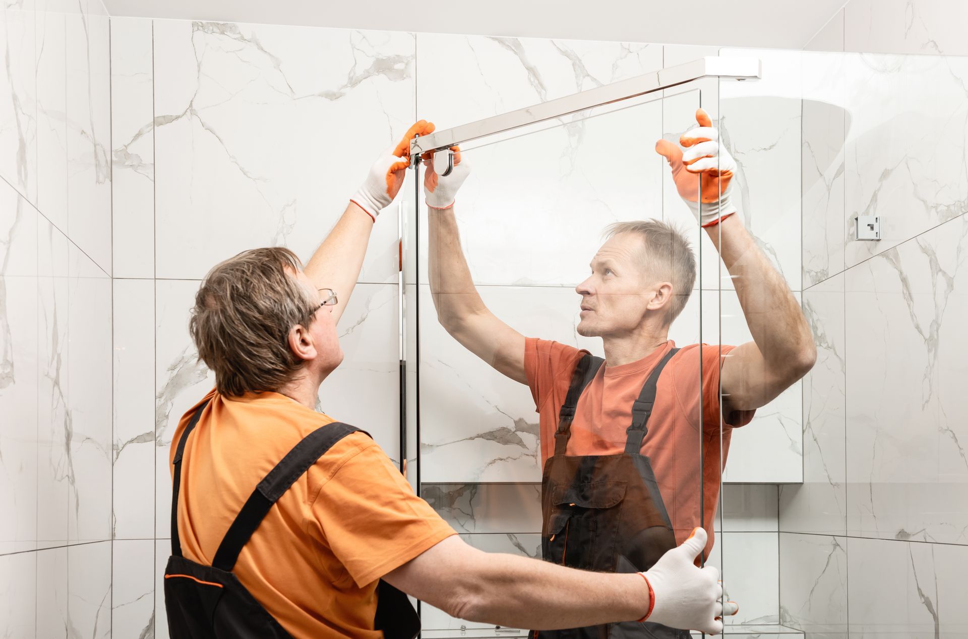 A pair of male workers install a shower door inside a bathroom. A pair of male workers install a shower door inside a bathroom.