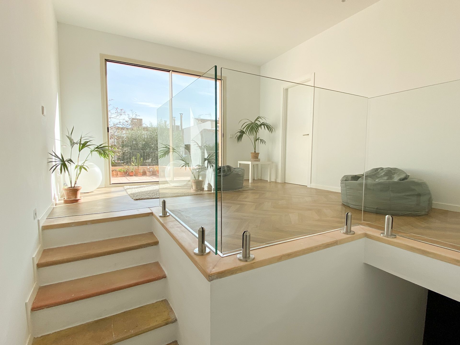 A living room with stairs leading up to the second floor and a glass railing.