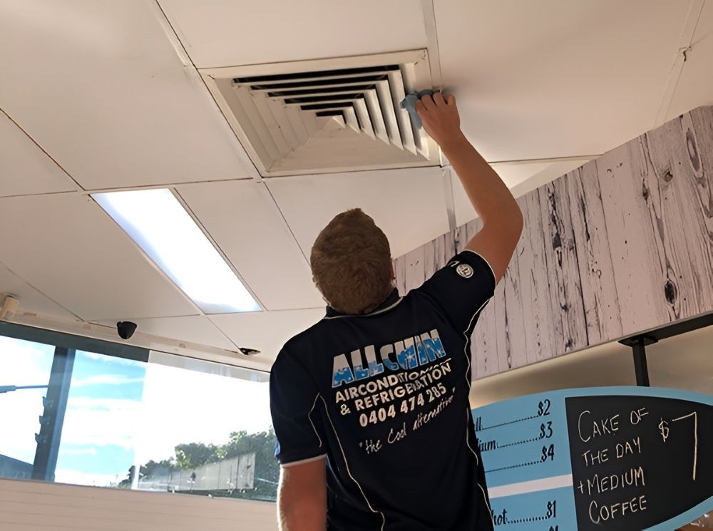 A Person In A Blue Shirt Cleaning An Air Vent In A Building's Ceiling — Allchin Airconditioning & Refrigeration Electrical in Caloundra, QLD
