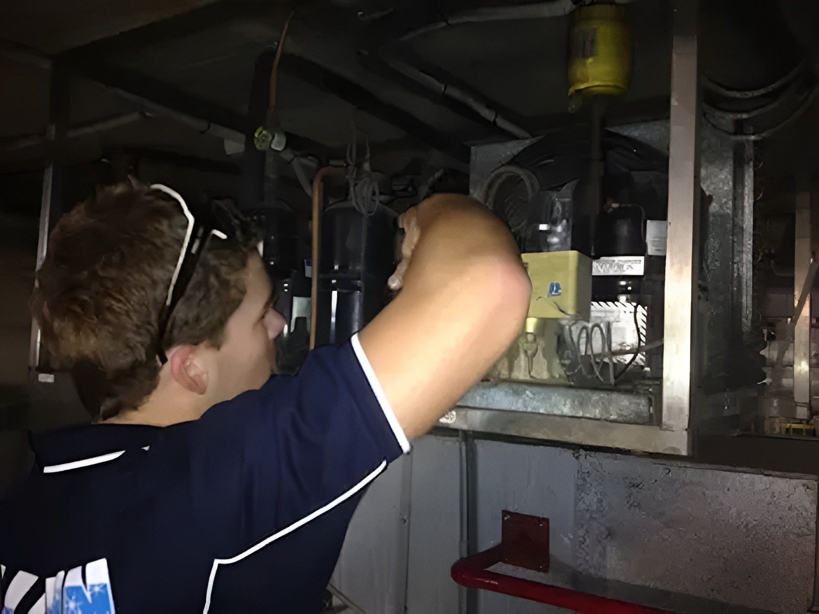A Person, Wearing Safety Glasses, Works On An Hvac System In A Dim Setting — Allchin Airconditioning & Refrigeration Electrical in Caloundra, QLD