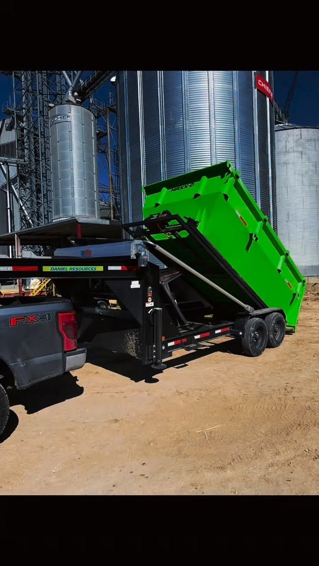 Daniel Resources black pickup truck delivering a green roll-off dumpster