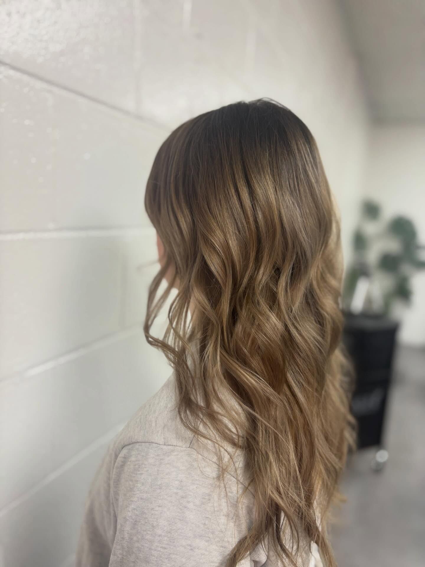 Side view of long wavy brown hair with blonde highlights in a softly lit salon setting