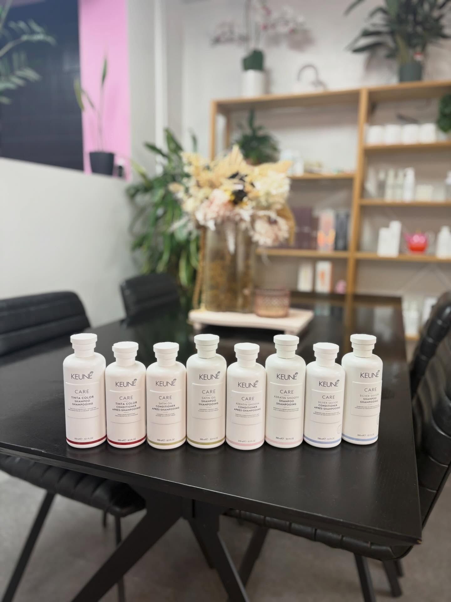 Eight white skincare bottles lined up on a black table in a modern office lobby