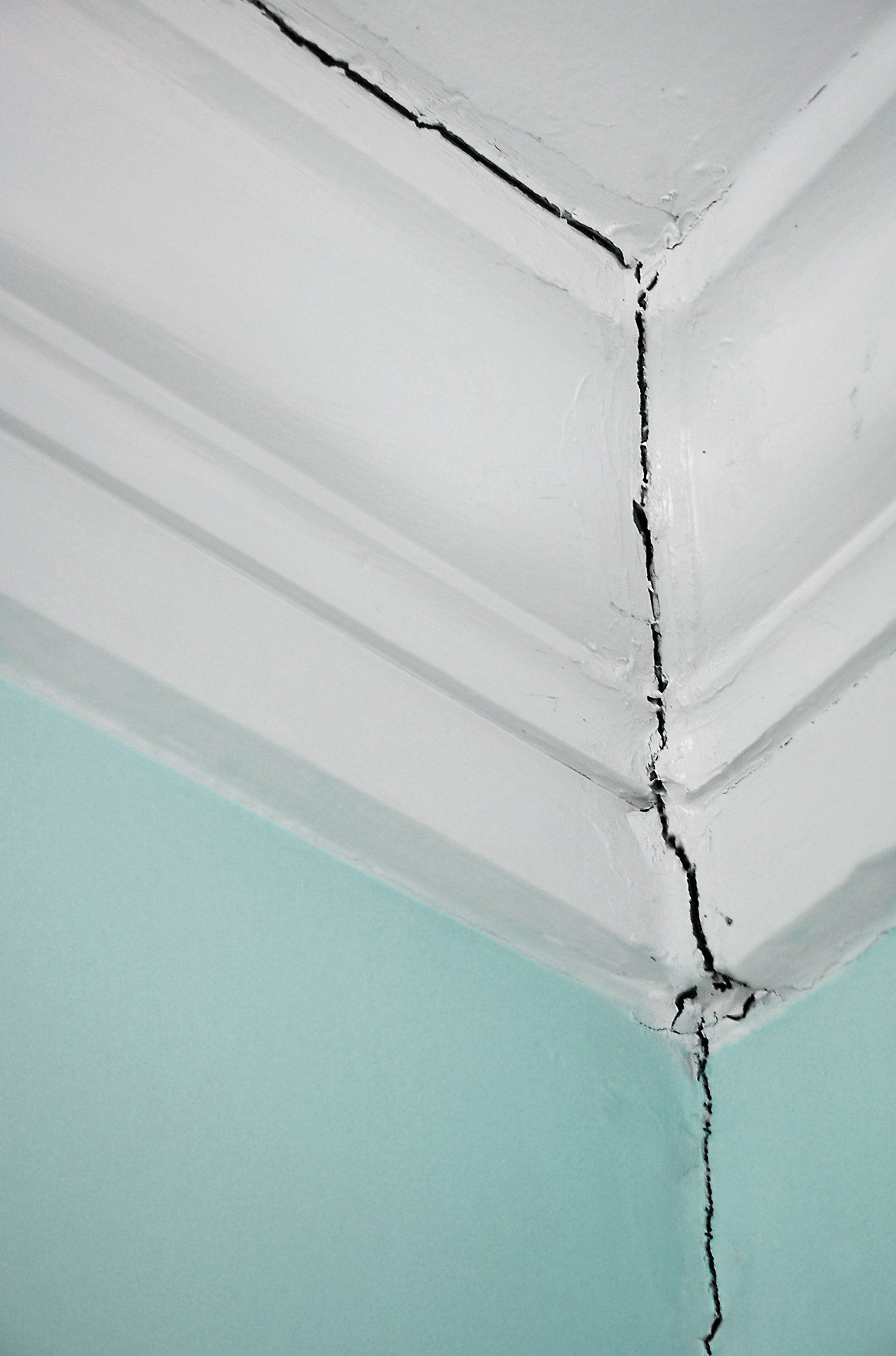 A large crack running vertically through the corner where the wall meets the decorative ceiling crown molding.