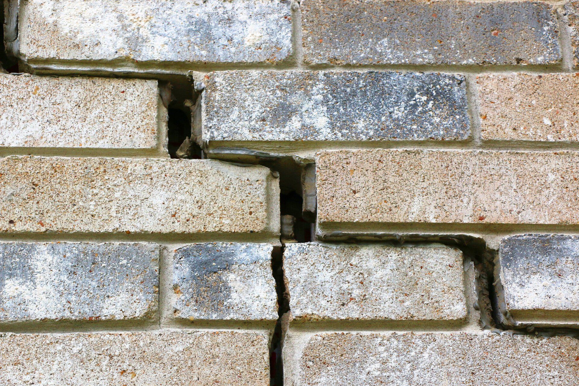 A close-up of a brick wall showing a large, jagged, step-shaped crack running through the mortar and bricks.