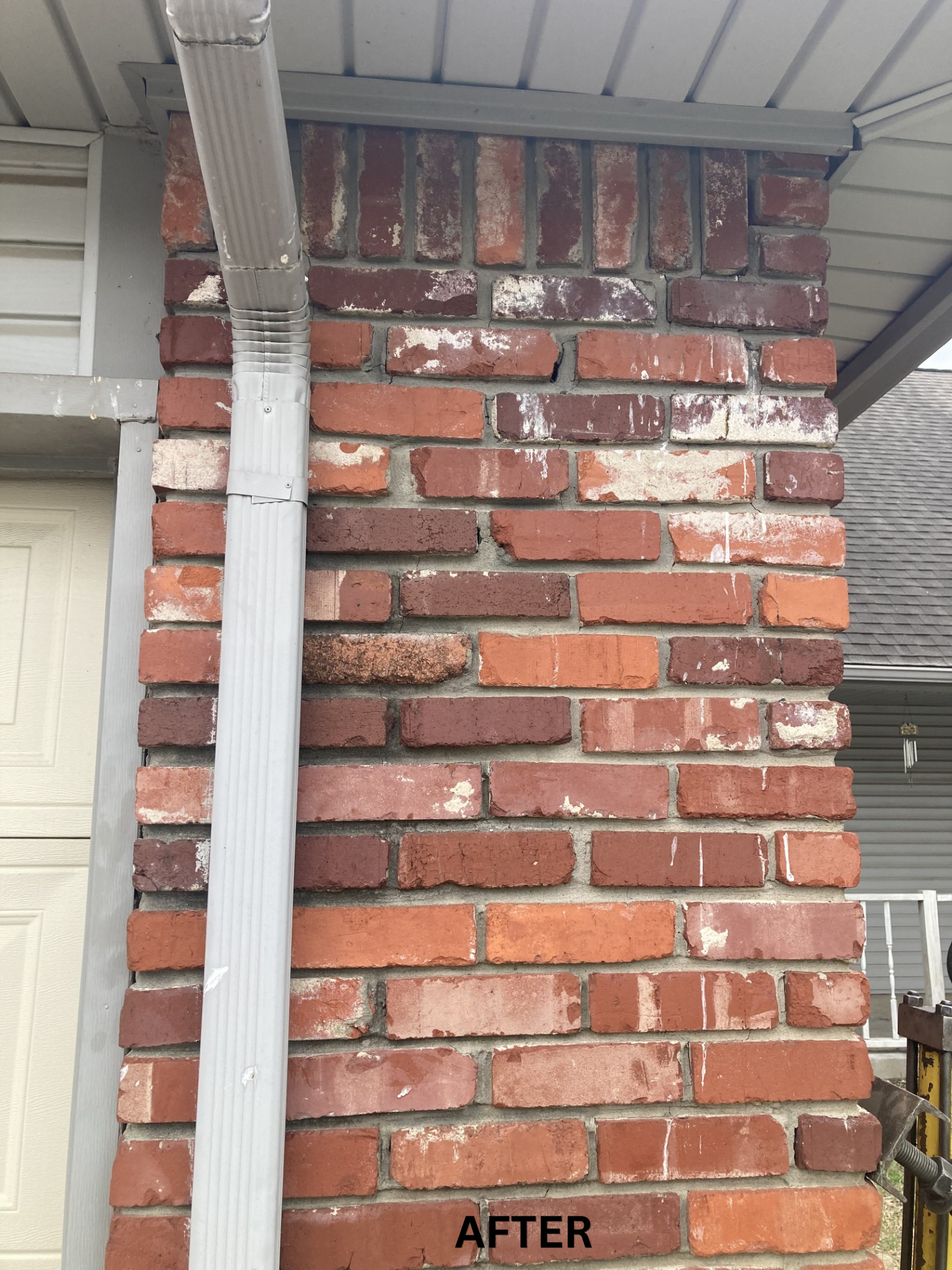 Close-up of a red brick porch column with white mortar and a white downspout under the roof eave.