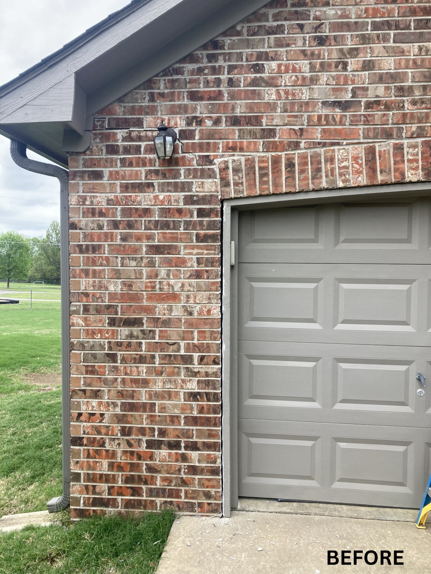 Brick garage exterior with gray door and a wall-mounted light, labeled “BEFORE”