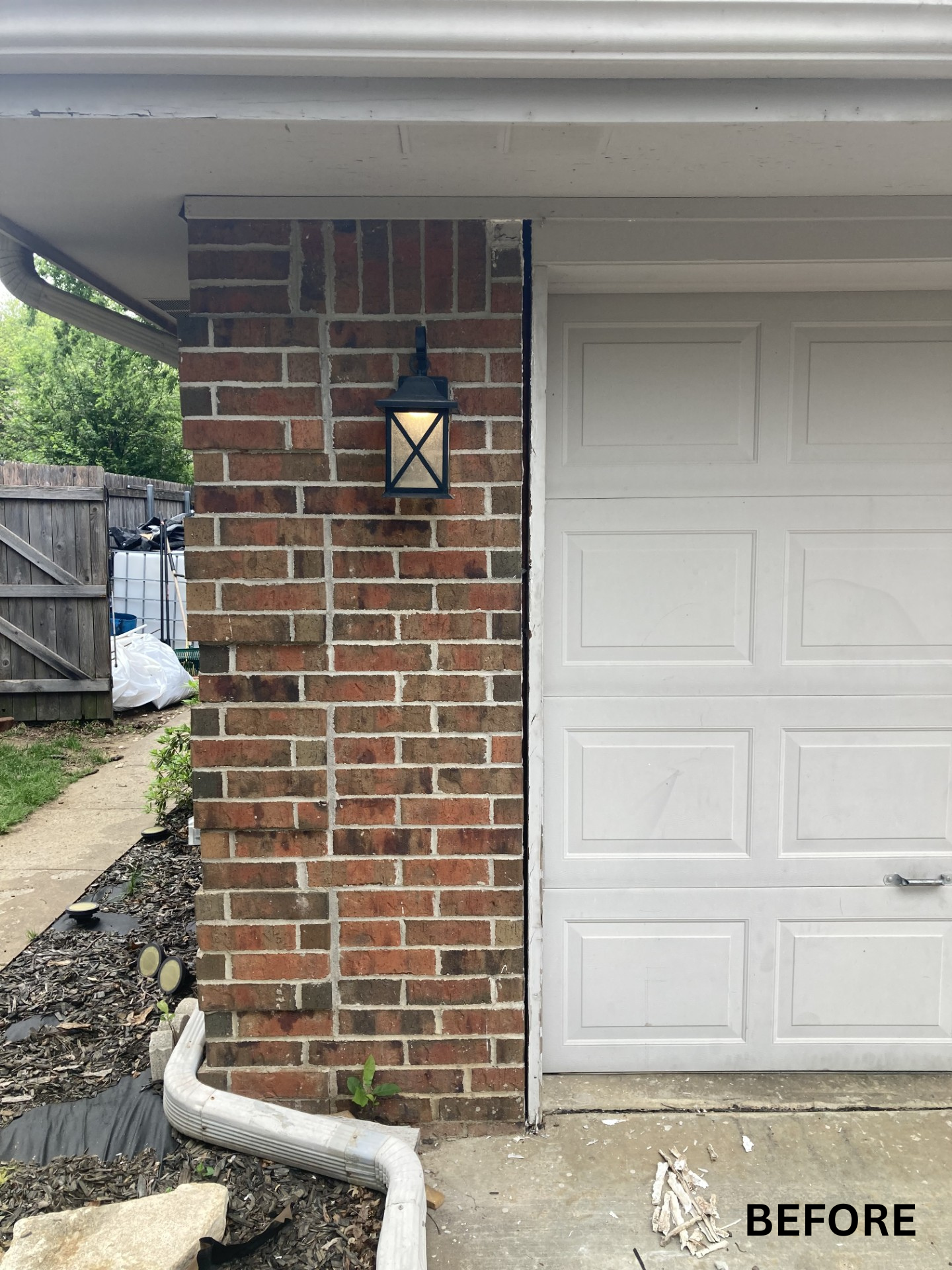 Brick porch column beside white garage door with wall lantern and downspout; side yard visible.