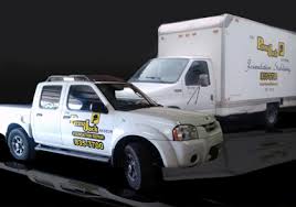 A white pickup truck and a white box truck from Ram Jack Foundation Repair parked against a solid dark background.