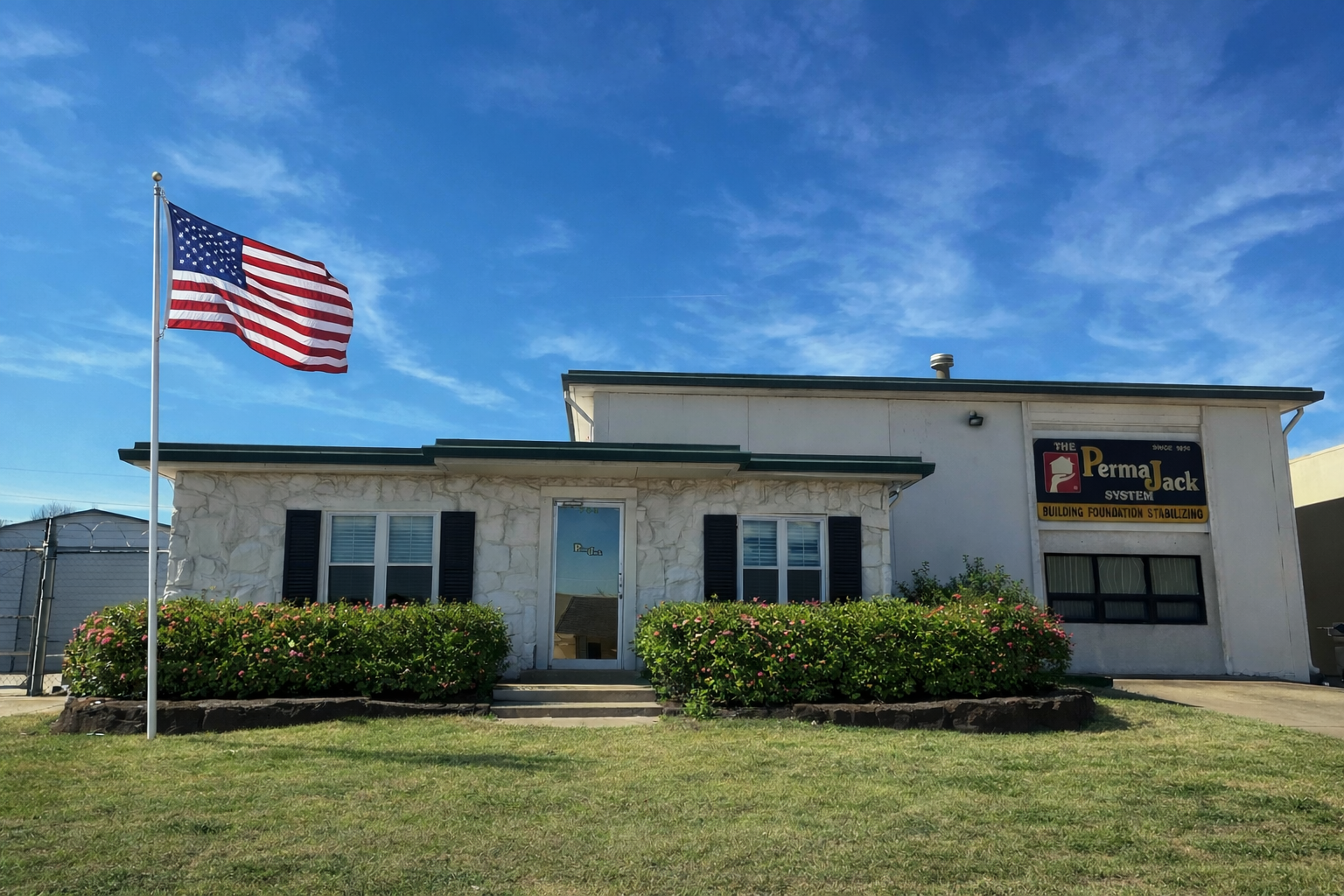 A one-story white stone commercial building with a US flag, dark shutters, and a 