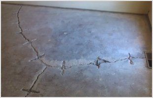 A concrete floor with a semi-circular crack repaired with metal staples inserted across the break.