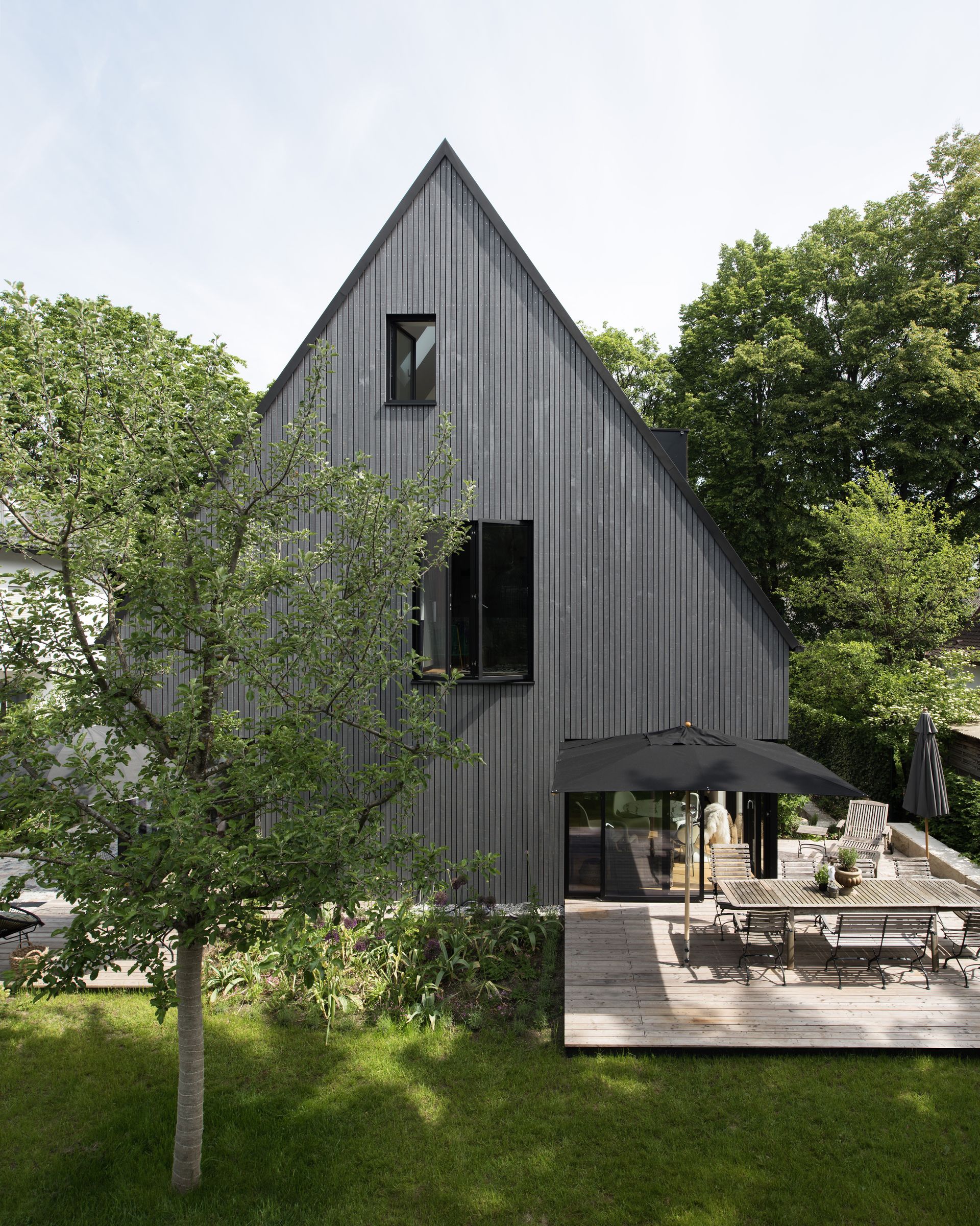 Modern gray A-frame house with patio, surrounded by green trees and lawn