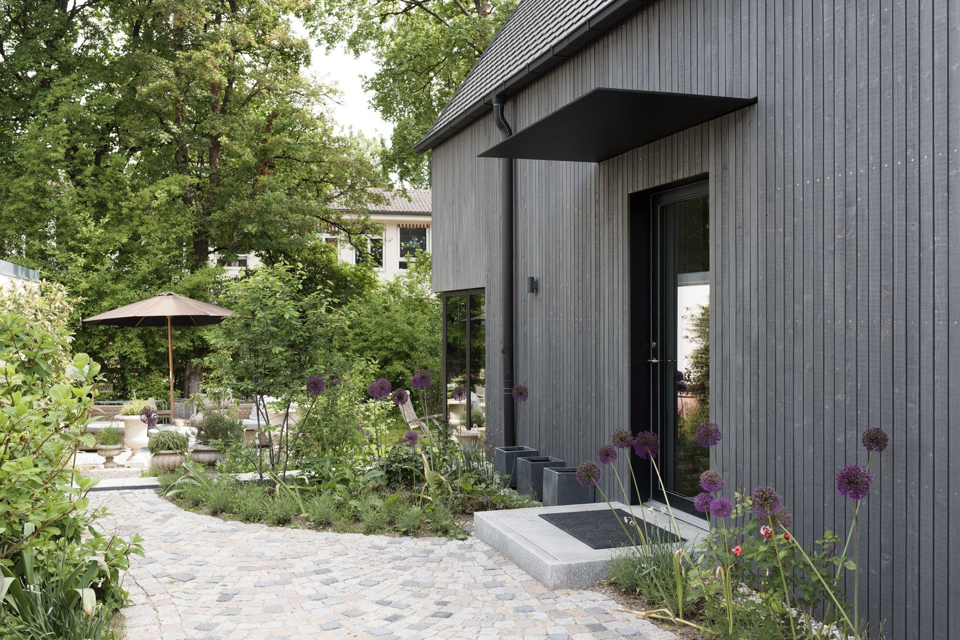Modern gray house with a garden path, lush greenery, and a patio umbrella