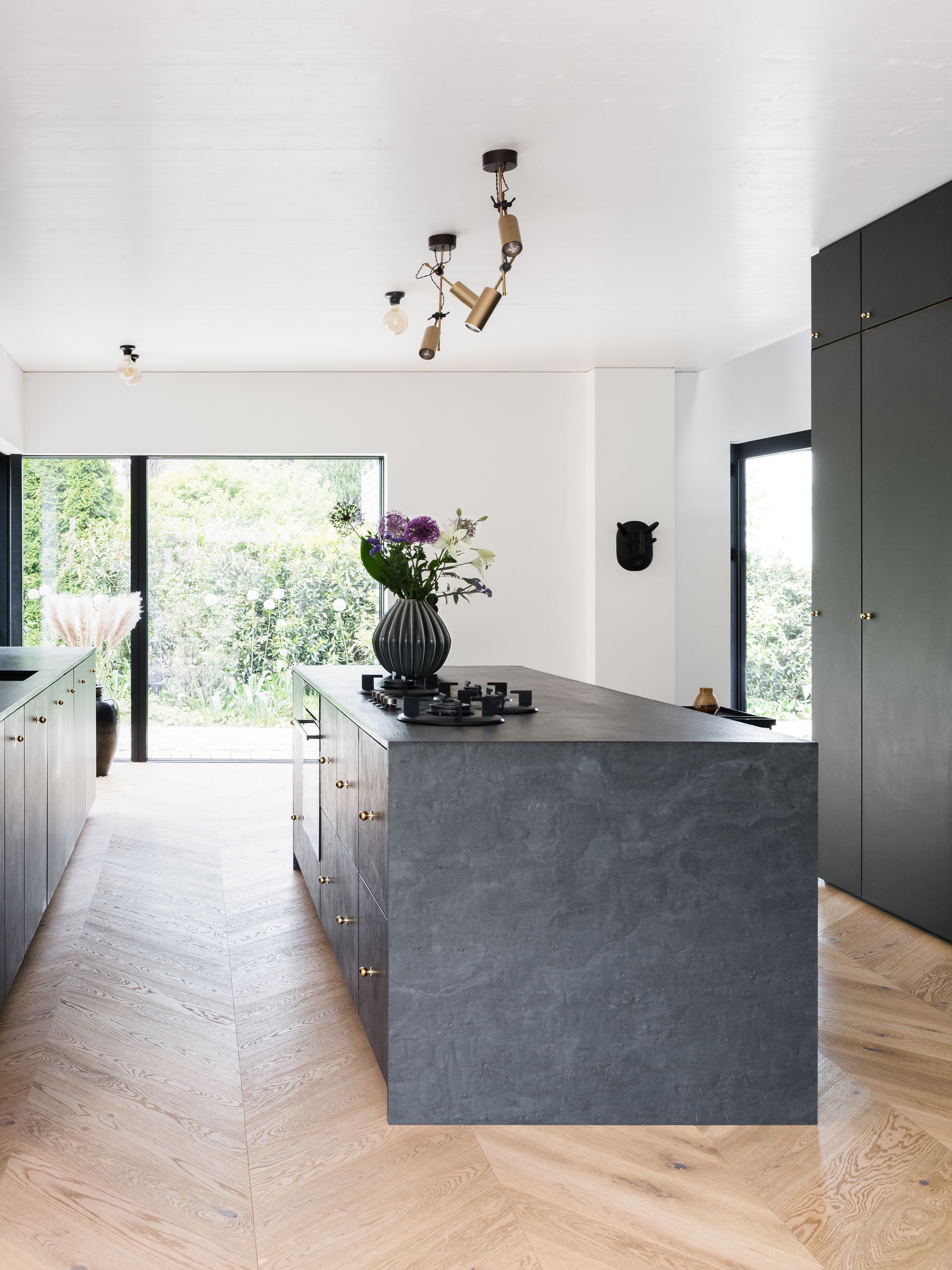 Modern kitchen with a gray island, flowers, and large windows overlooking greenery