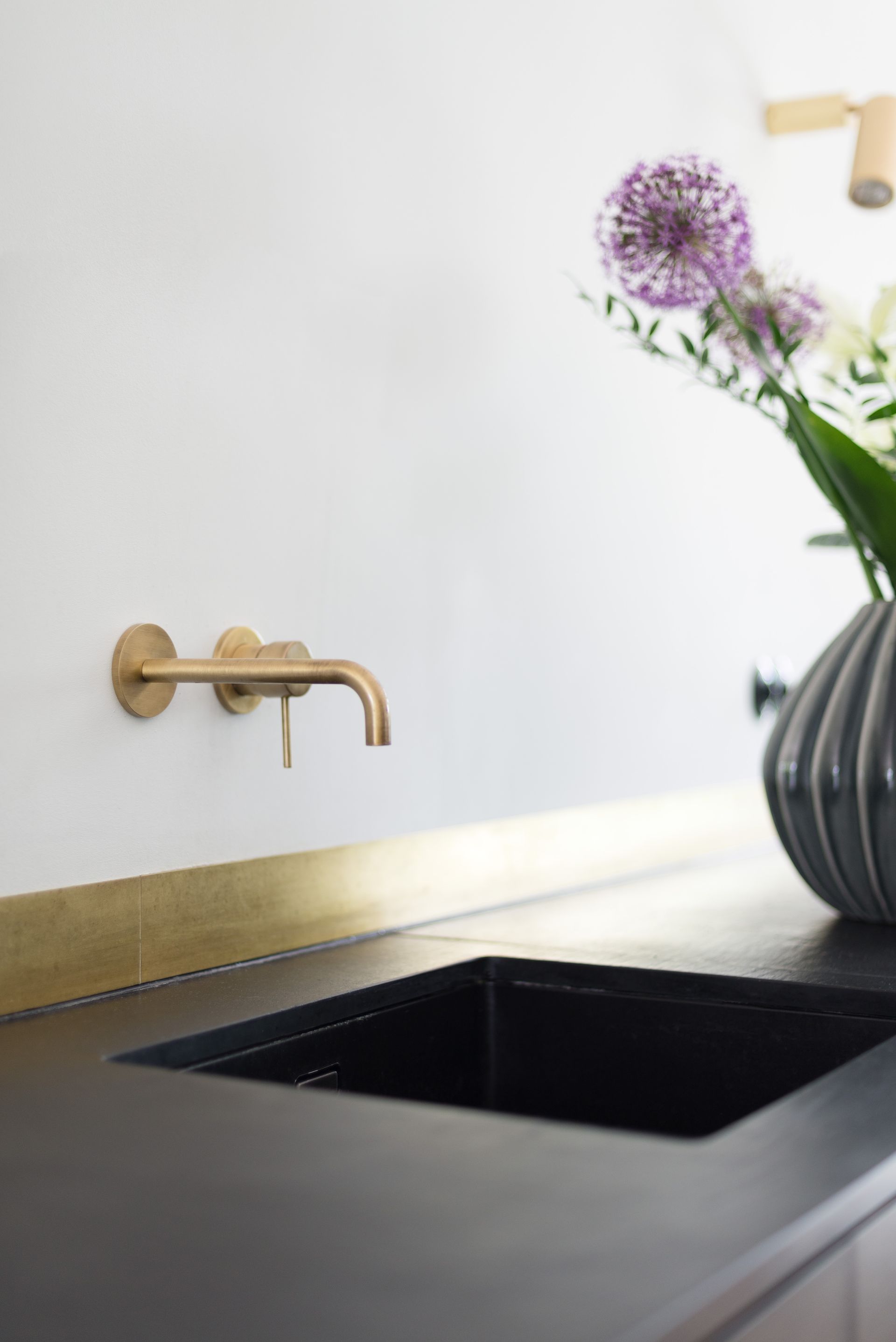 Modern kitchen sink with matte black countertop, gold faucet, and purple flowers in a vase