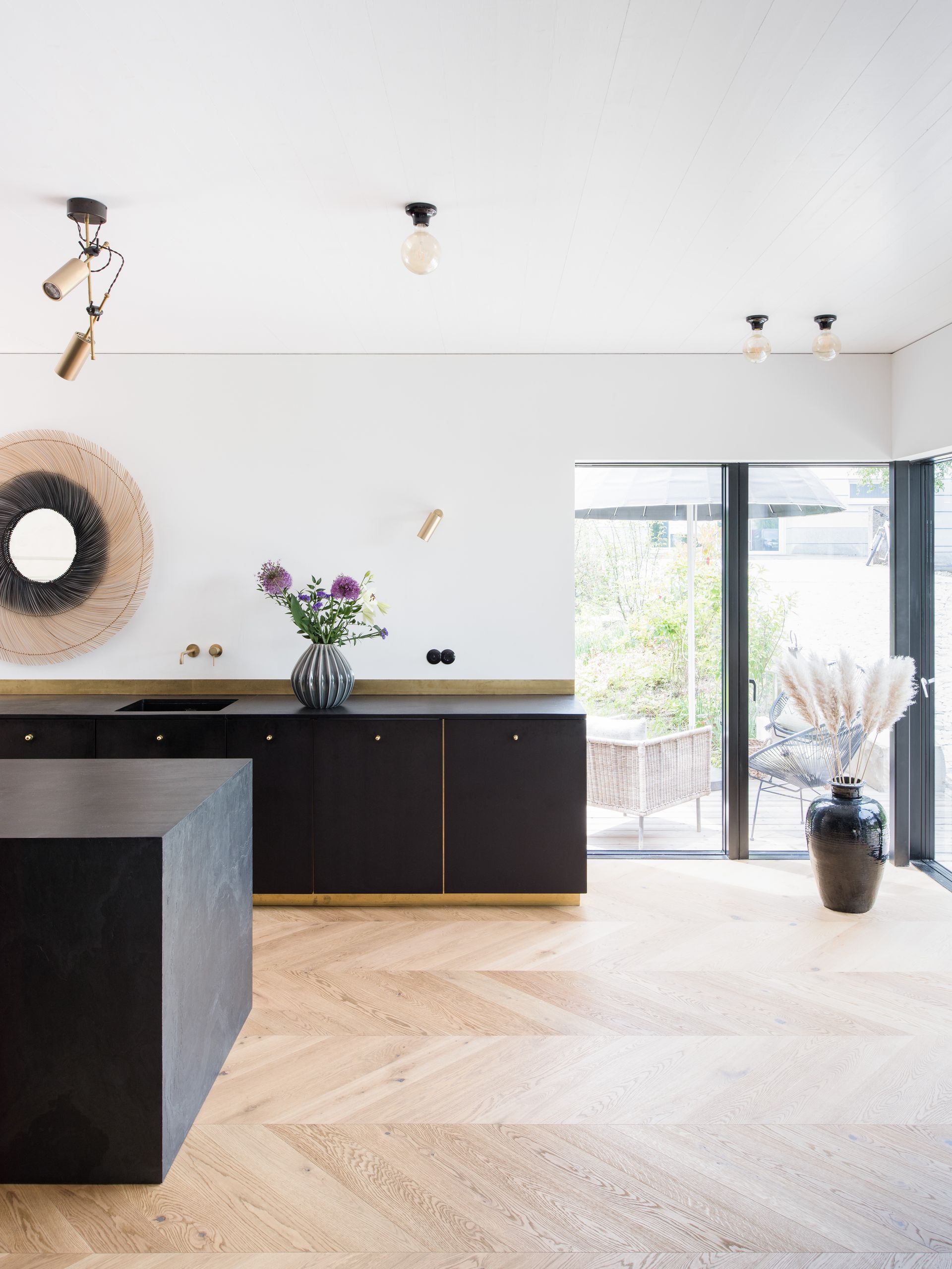 Modern minimalist living room with black cabinet, round wall mirror, flowers, and sliding glass doors.
