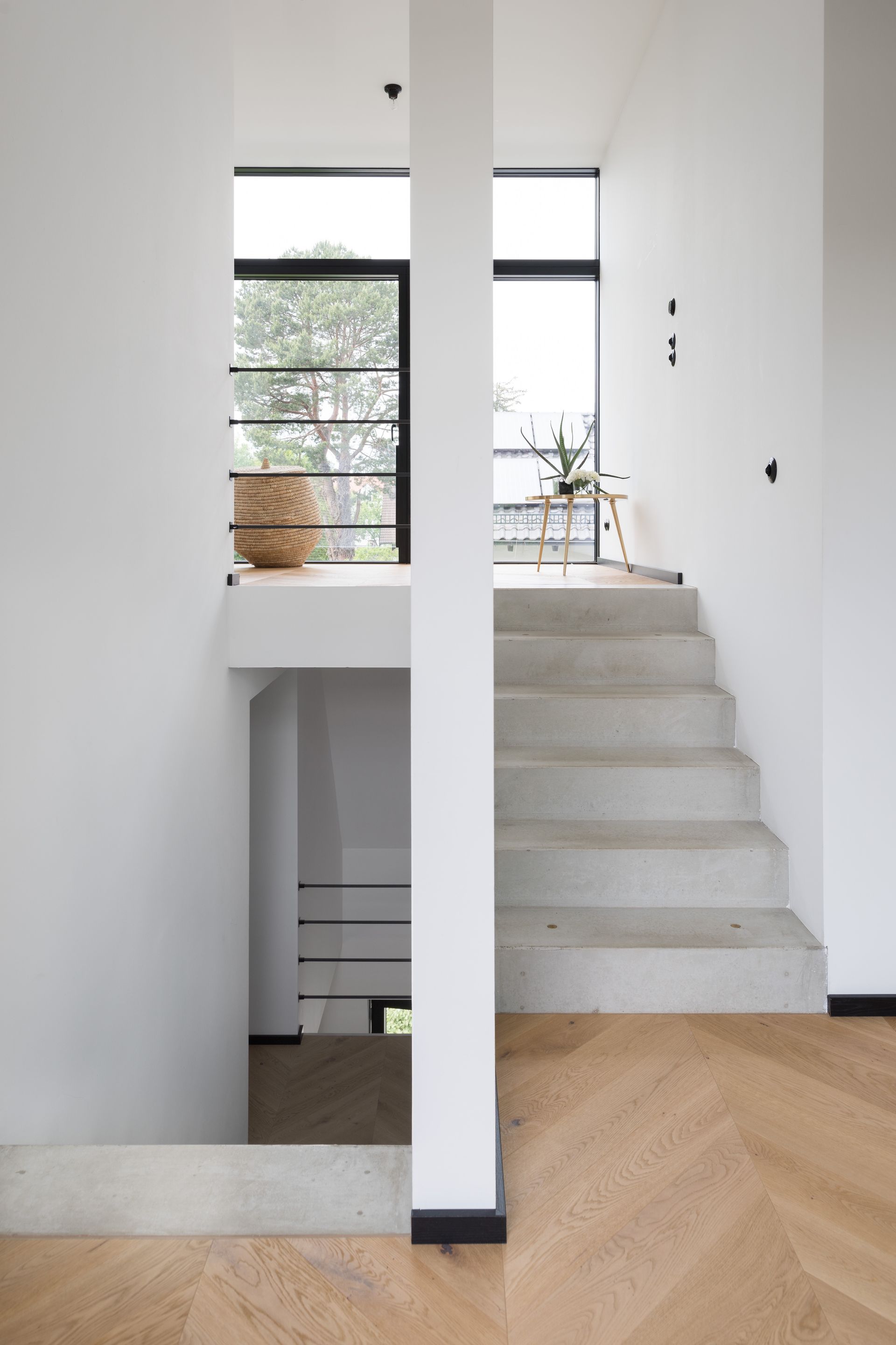 Minimalist staircase and hallway with white walls, black-framed windows, and light wood flooring