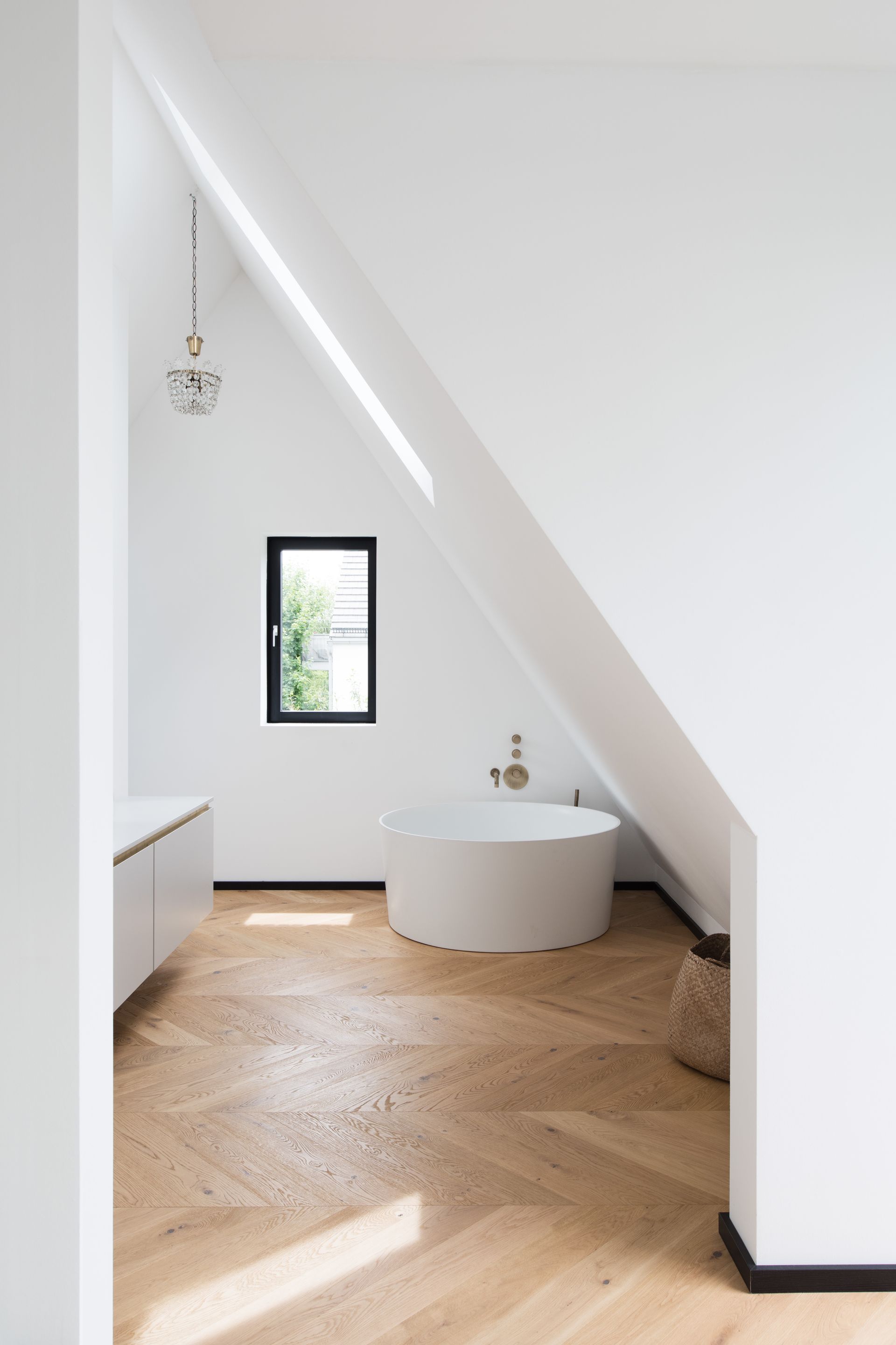 Minimalist white attic room with sloped ceiling, small window, pendant light, and a round white table on wood floor