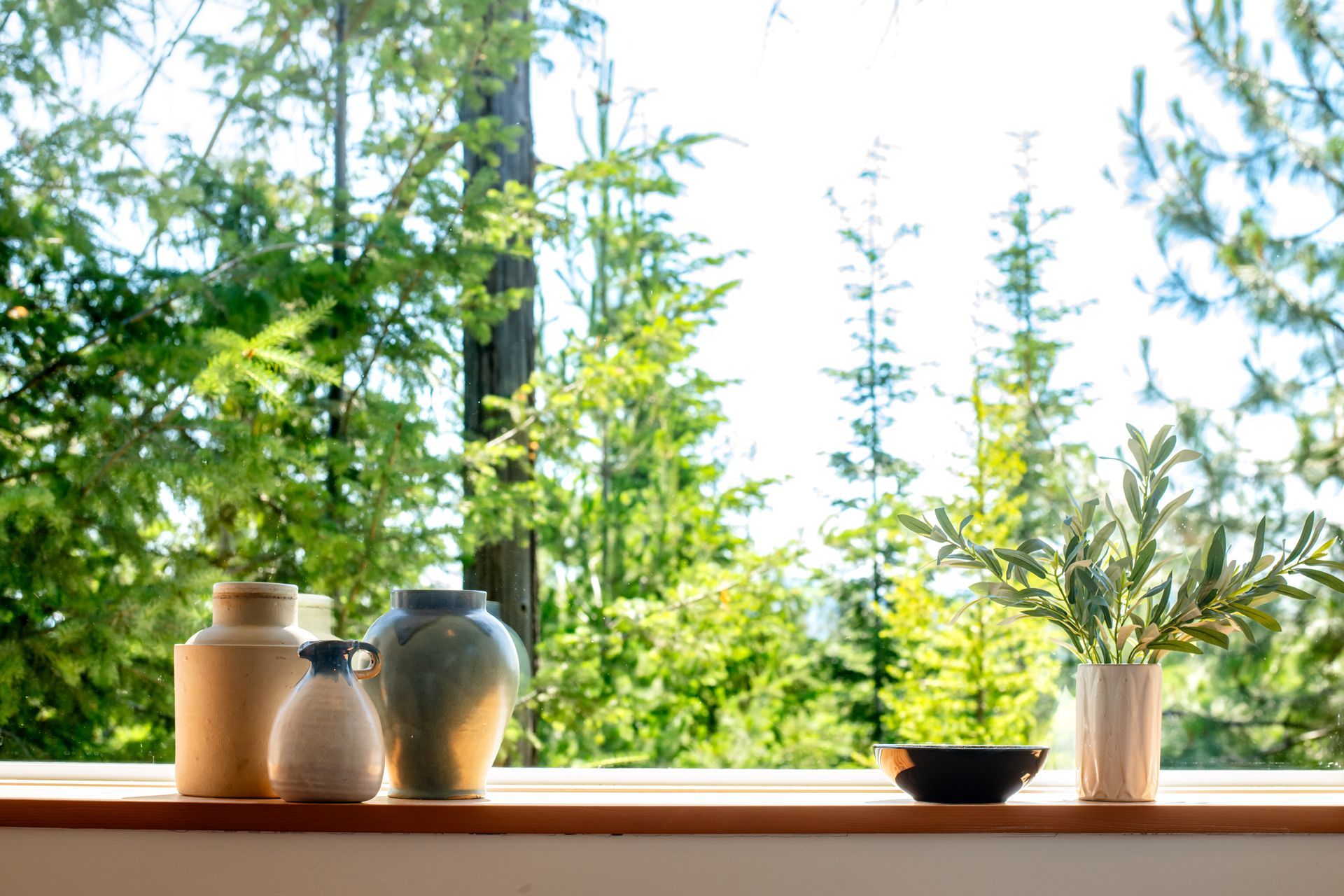 Ceramic jars and a small bowl on a wooden windowsill, with green trees outside.