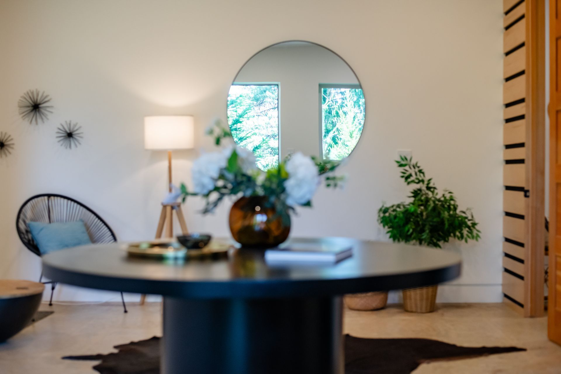 Modern living room with round table, lamp, mirror, black chairs, and potted plants