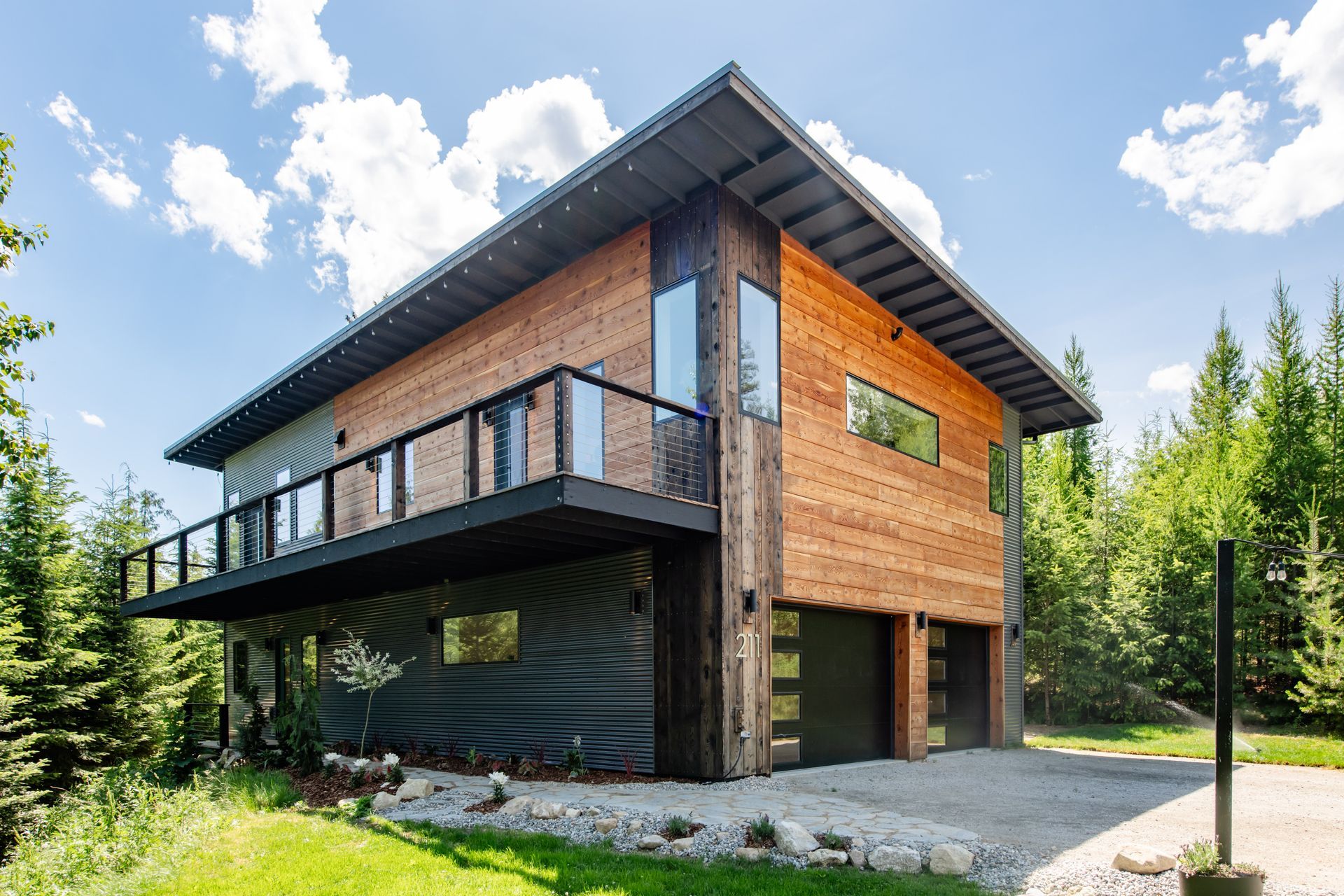 Modern wooden house with a black balcony and sloped roof in a sunny forest setting
