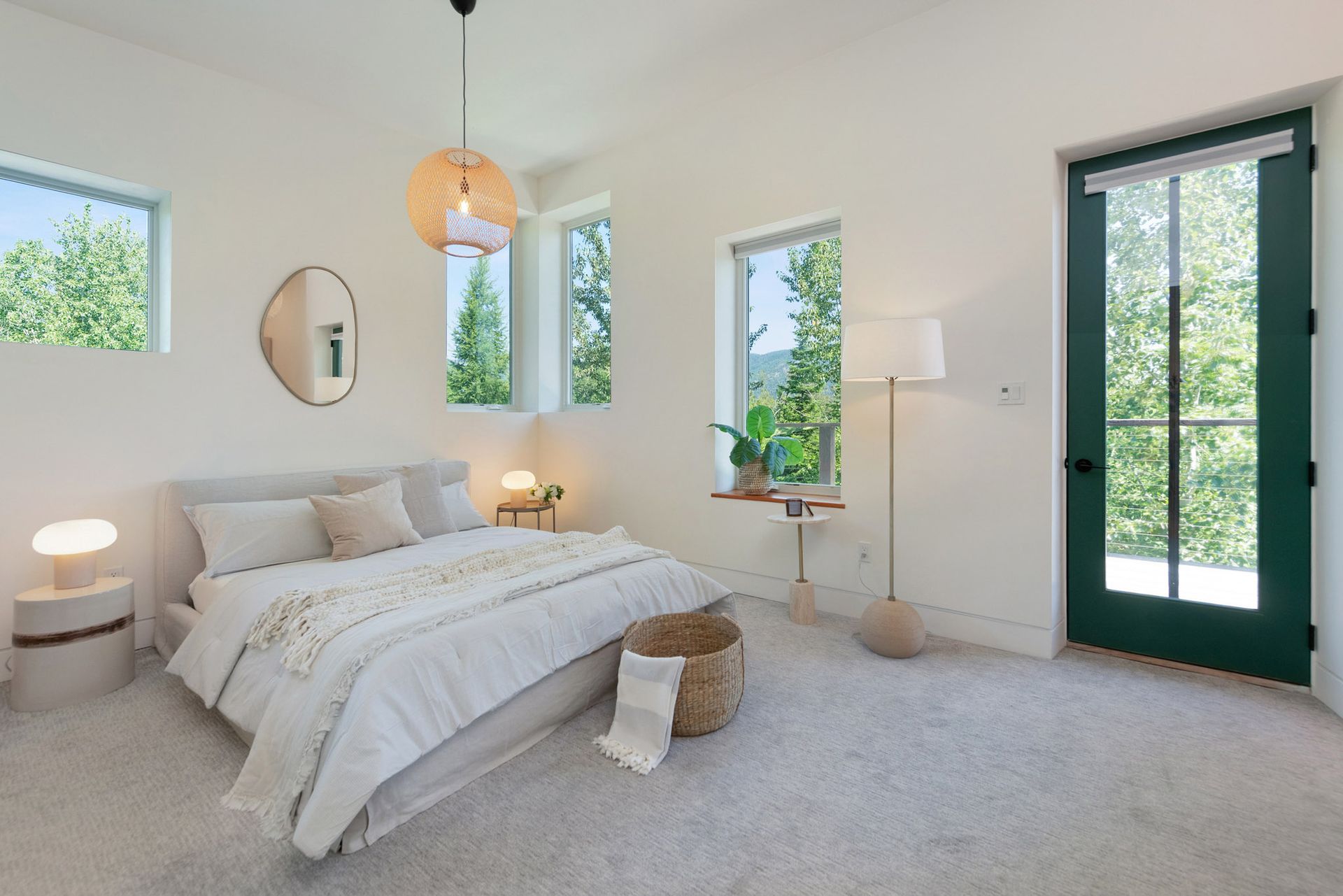 Bright bedroom with a white bed, beige carpet, large windows, and black French doors overlooking greenery