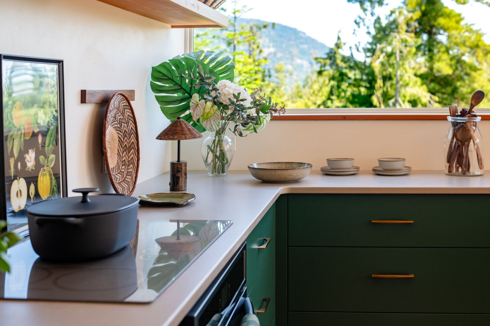 Modern kitchen with green cabinets, black pot on stovetop, and plants on a bright counter